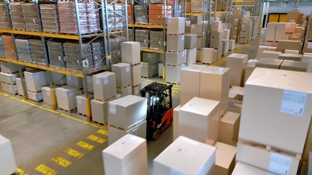 Logistique d'entrepôt : chariot élévateur gérant des palettes. Un chariot élévateur se déplace rapidement parmi des piles de grands cartons emballés sur palettes dans un vaste entrepôt de logistique.